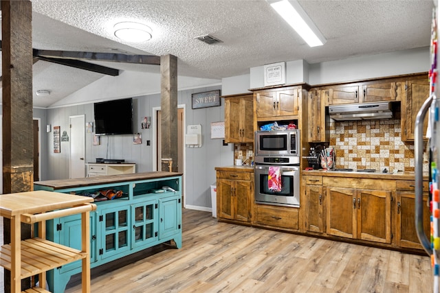 kitchen with light wood-type flooring, appliances with stainless steel finishes, a textured ceiling, and vaulted ceiling