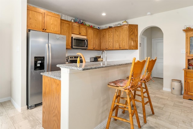 kitchen with appliances with stainless steel finishes, sink, light stone counters, a kitchen breakfast bar, and decorative backsplash