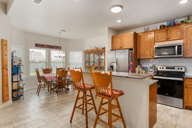 kitchen with a center island with sink, appliances with stainless steel finishes, a kitchen breakfast bar, and decorative light fixtures