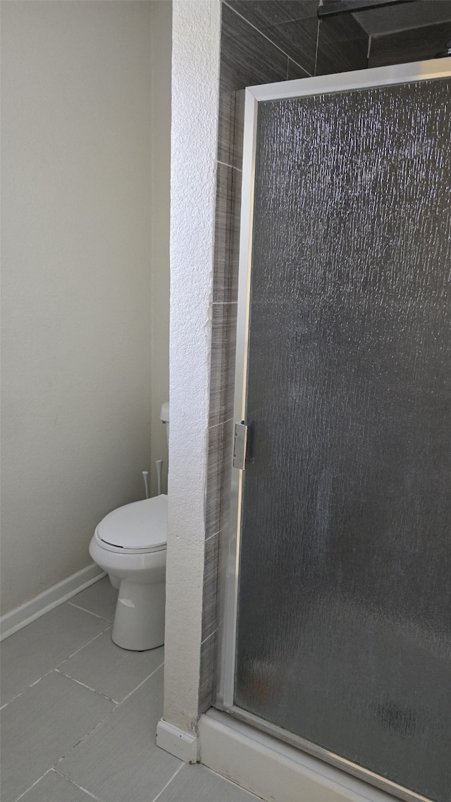 bathroom with a shower with shower door, tile patterned floors, and toilet