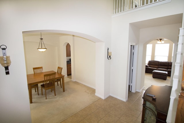 dining area featuring light colored carpet, a towering ceiling, and ceiling fan