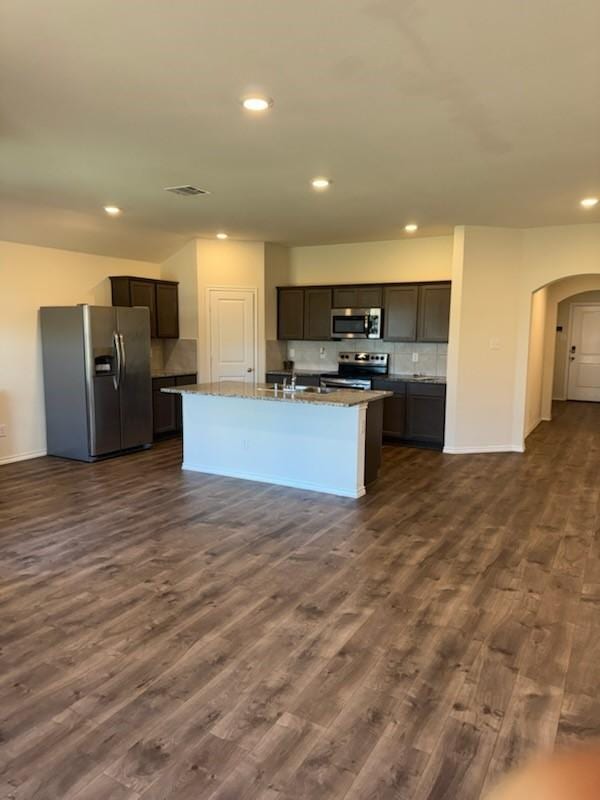kitchen featuring appliances with stainless steel finishes, arched walkways, recessed lighting, dark wood-type flooring, and tasteful backsplash