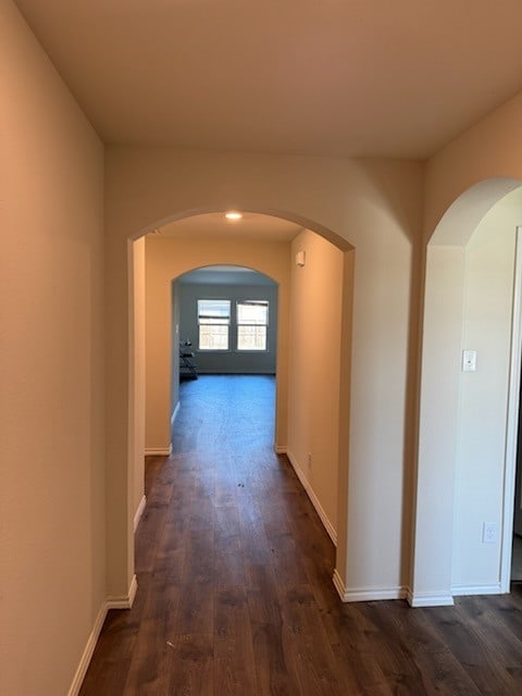 hall with arched walkways, dark wood finished floors, and baseboards