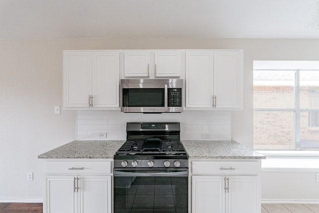 kitchen with tasteful backsplash, range with gas cooktop, light stone counters, and white cabinets