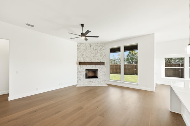 unfurnished living room with hardwood / wood-style floors, a stone fireplace, and ceiling fan