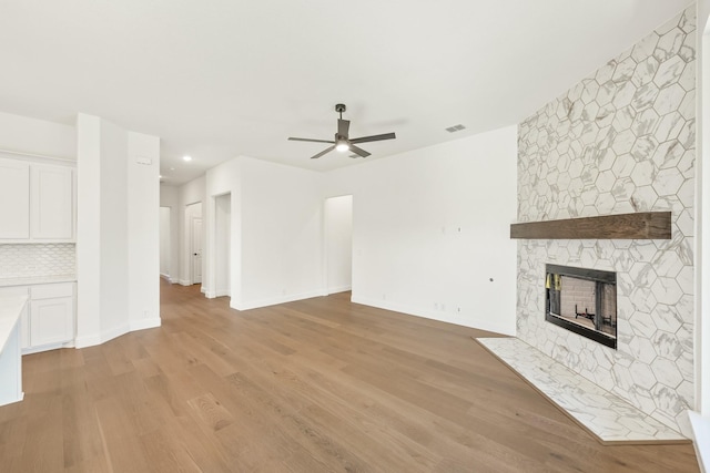 unfurnished living room with ceiling fan, a fireplace, and light hardwood / wood-style flooring