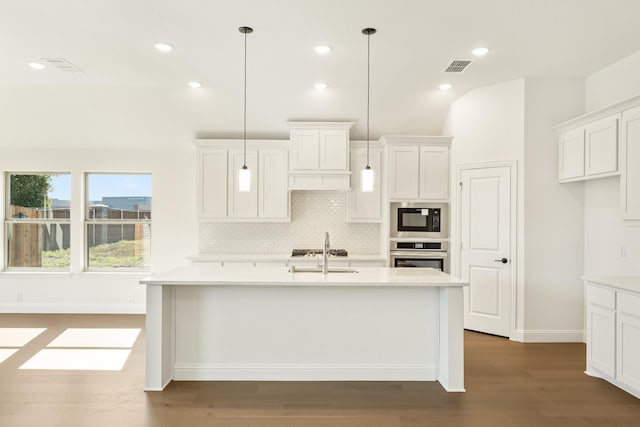 kitchen featuring a kitchen island with sink, hardwood / wood-style floors, oven, and decorative light fixtures