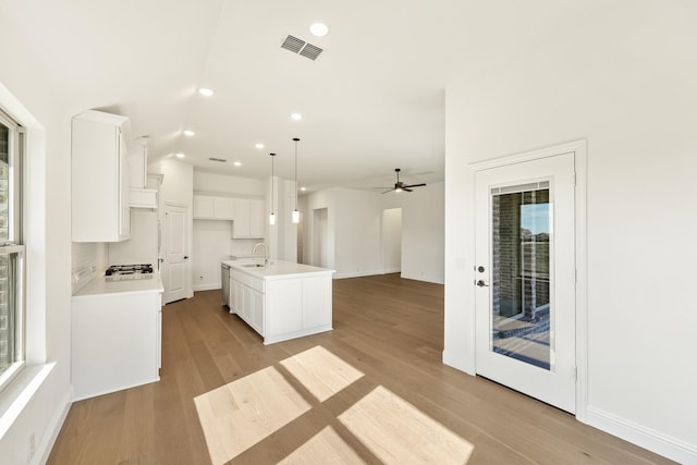 kitchen featuring ceiling fan, white cabinets, light hardwood / wood-style floors, hanging light fixtures, and an island with sink