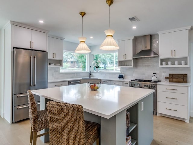 kitchen featuring a kitchen island, a breakfast bar, white cabinetry, premium appliances, and wall chimney exhaust hood