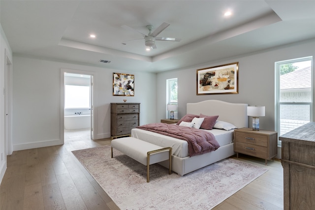 bedroom featuring ceiling fan, ensuite bathroom, a tray ceiling, and light hardwood / wood-style floors