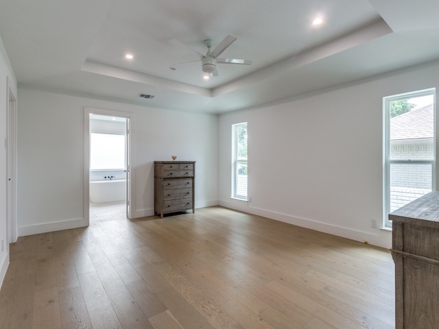 unfurnished bedroom featuring light hardwood / wood-style floors, a tray ceiling, connected bathroom, and ceiling fan