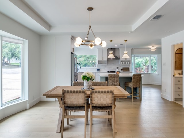 dining area featuring a tray ceiling, plenty of natural light, a chandelier, and light wood-type flooring