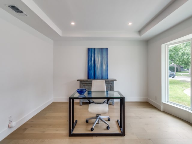 home office with a wealth of natural light, light hardwood / wood-style floors, and a raised ceiling