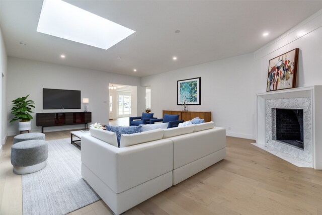 living room with a high end fireplace, a skylight, and light hardwood / wood-style flooring