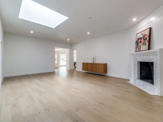 unfurnished living room featuring a premium fireplace, a skylight, and light hardwood / wood-style flooring