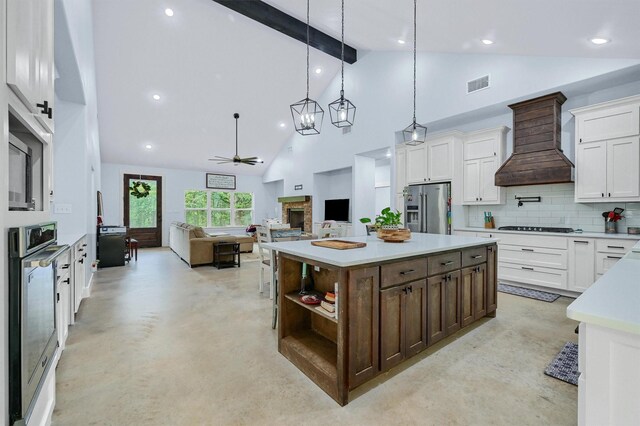 kitchen featuring stainless steel appliances, backsplash, beamed ceiling, custom range hood, and a kitchen island