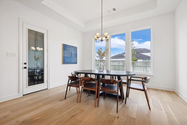 dining room featuring light hardwood / wood-style flooring, a wealth of natural light, a notable chandelier, and a raised ceiling