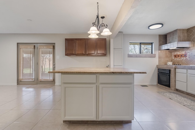 kitchen featuring white cabinets, decorative backsplash, light tile patterned floors, black oven, and a chandelier