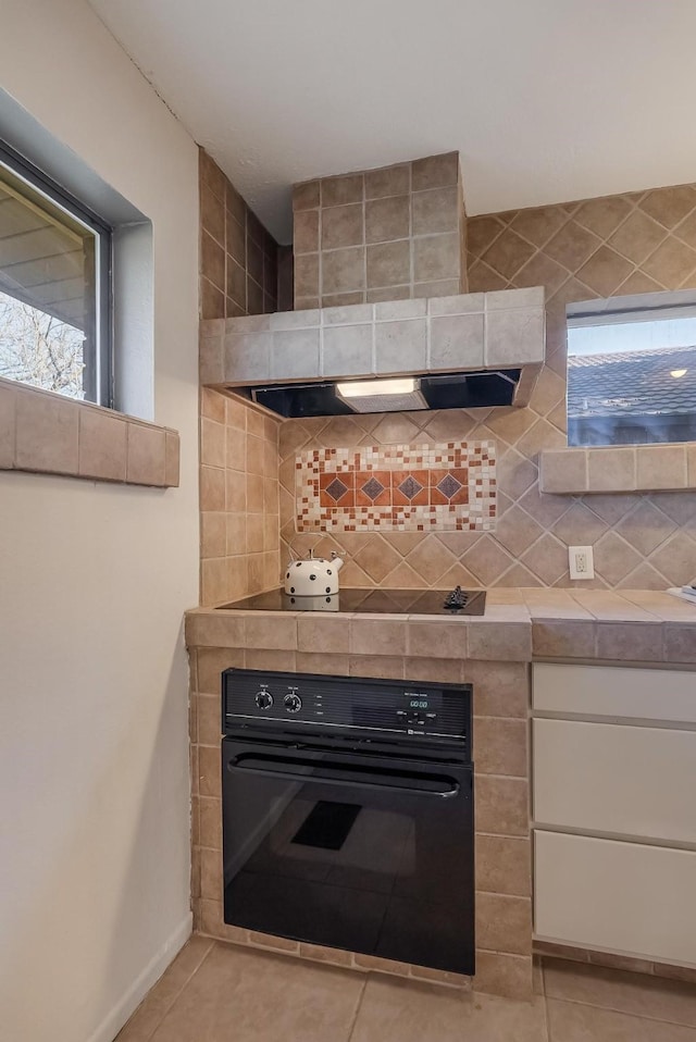 kitchen with white cabinetry, decorative backsplash, light tile patterned floors, black appliances, and custom exhaust hood