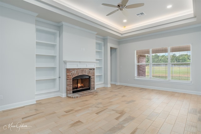 unfurnished living room featuring ceiling fan, light wood-type flooring, a fireplace, and a tray ceiling