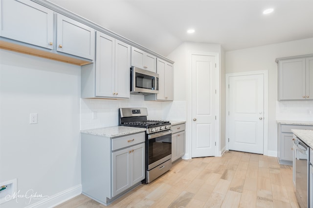 kitchen featuring stainless steel appliances, decorative backsplash, light wood-type flooring, gray cabinets, and light stone counters