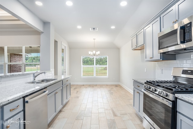 kitchen featuring tasteful backsplash, an inviting chandelier, appliances with stainless steel finishes, light stone counters, and sink