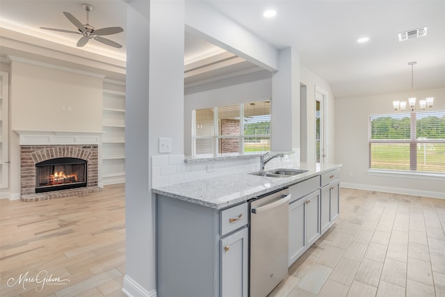 kitchen with tasteful backsplash, ceiling fan with notable chandelier, dishwasher, a tray ceiling, and sink