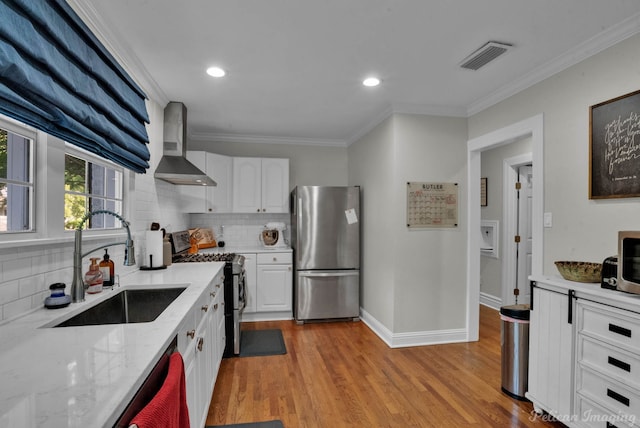 kitchen with appliances with stainless steel finishes, backsplash, white cabinetry, light hardwood / wood-style flooring, and wall chimney range hood