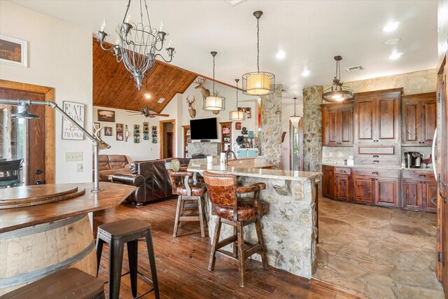 kitchen featuring light stone counters, ceiling fan, high vaulted ceiling, light hardwood / wood-style floors, and a breakfast bar