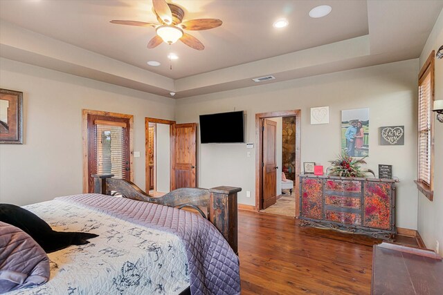 bedroom with ceiling fan, ensuite bathroom, hardwood / wood-style floors, and a tray ceiling