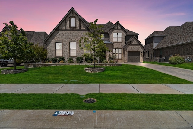 tudor home with a garage, a lawn, and central air condition unit