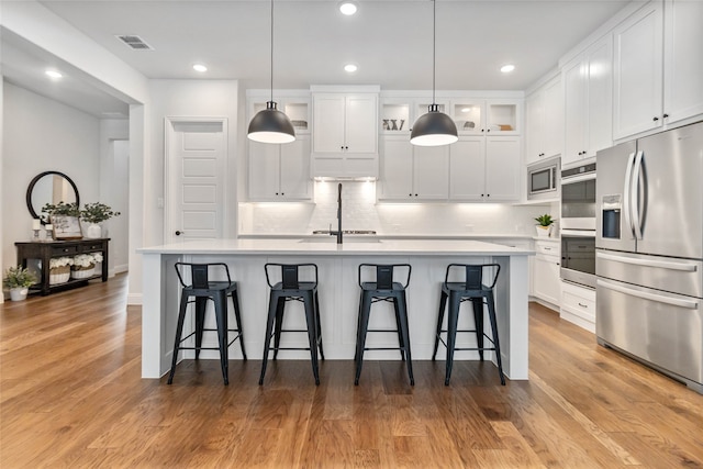 kitchen featuring stainless steel appliances, light hardwood / wood-style floors, a center island with sink, and white cabinets