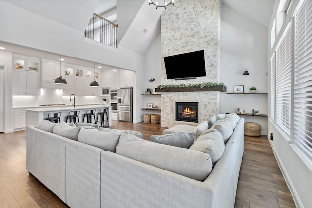 living room with wood-type flooring, a stone fireplace, sink, and high vaulted ceiling