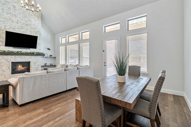 dining area with light wood-type flooring, a fireplace, an inviting chandelier, and high vaulted ceiling