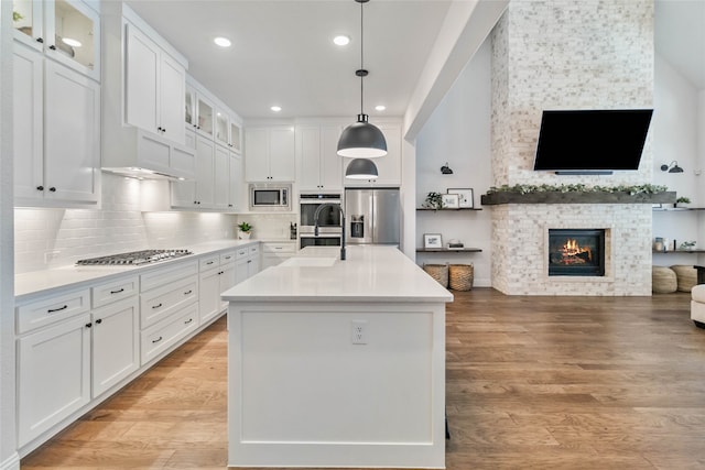 kitchen featuring appliances with stainless steel finishes, a fireplace, an island with sink, and white cabinets