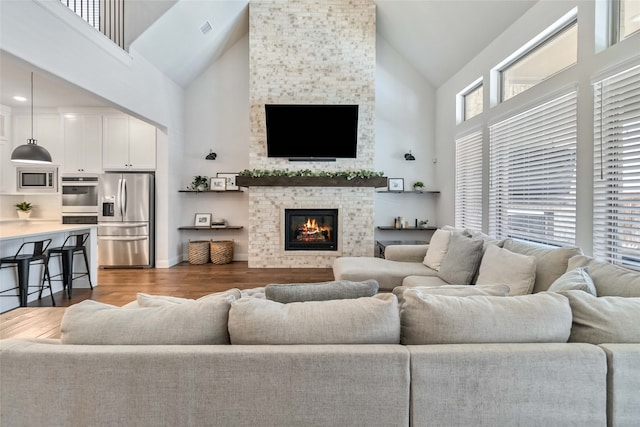 living room with a stone fireplace, dark hardwood / wood-style flooring, and high vaulted ceiling