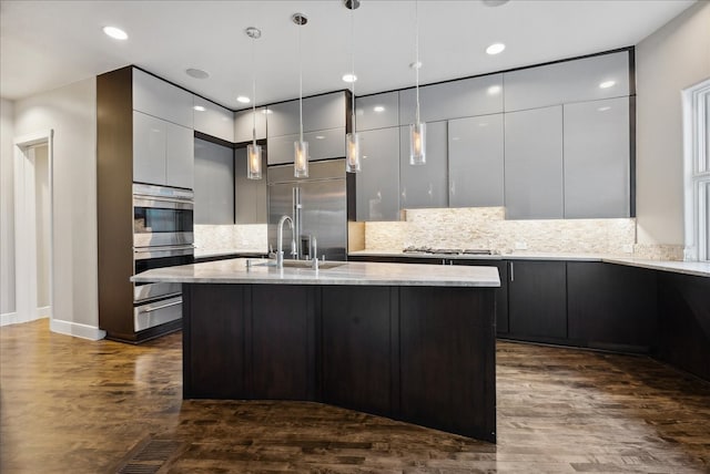 kitchen featuring appliances with stainless steel finishes, hanging light fixtures, light stone counters, and a kitchen island with sink