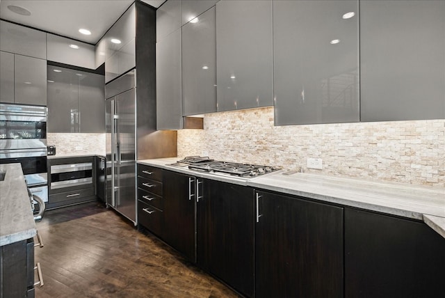 kitchen with stainless steel appliances, dark wood-type flooring, light stone counters, and backsplash