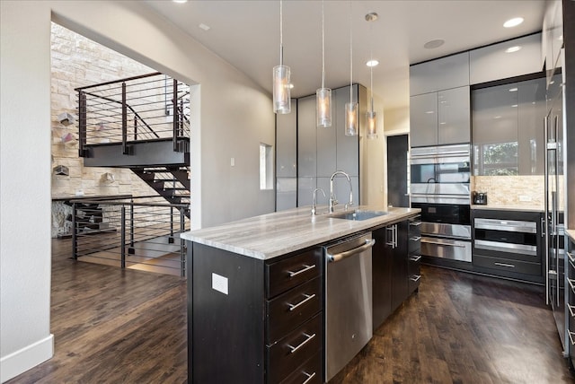 kitchen featuring stainless steel appliances, dark hardwood / wood-style flooring, hanging light fixtures, sink, and an island with sink