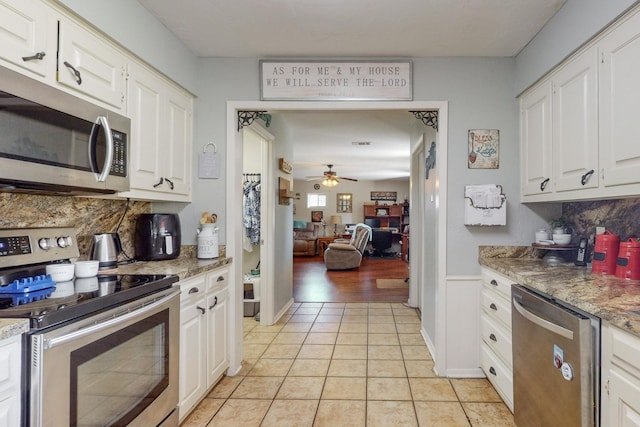 kitchen with stainless steel appliances, light stone countertops, decorative backsplash, light tile patterned floors, and white cabinetry