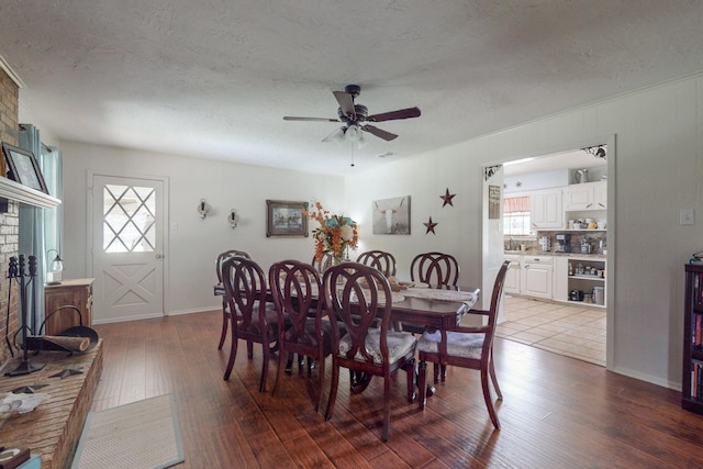 dining area featuring a brick fireplace, hardwood / wood-style flooring, ceiling fan, and a textured ceiling