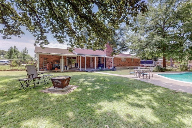 back of house with an outdoor fire pit, a patio, a fenced in pool, and a lawn