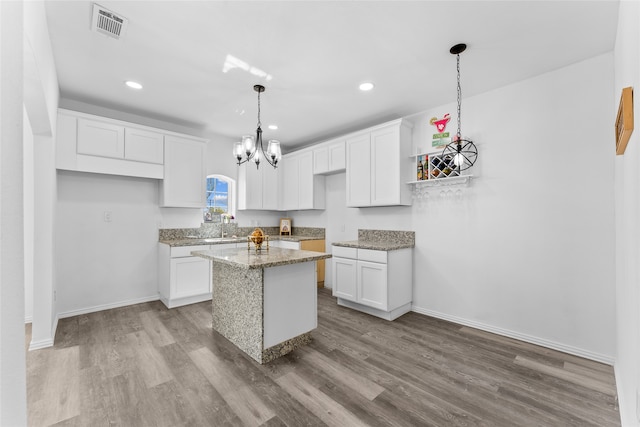 kitchen with pendant lighting, hardwood / wood-style flooring, light stone countertops, white cabinets, and a kitchen island