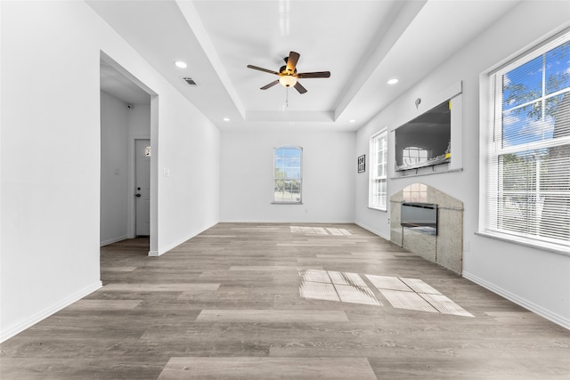 unfurnished living room with a tray ceiling, ceiling fan, and light wood-type flooring