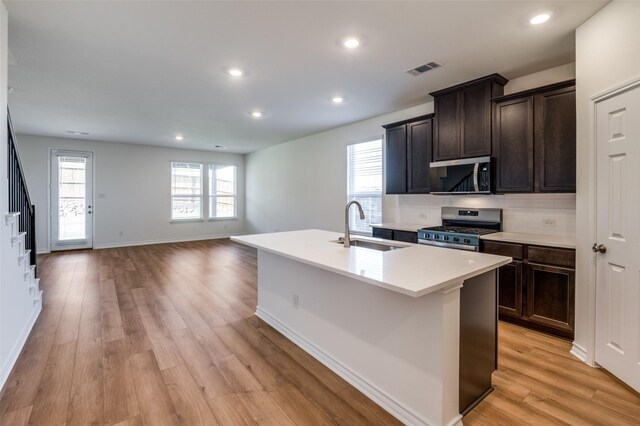 kitchen featuring sink, light hardwood / wood-style flooring, an island with sink, dark brown cabinets, and appliances with stainless steel finishes