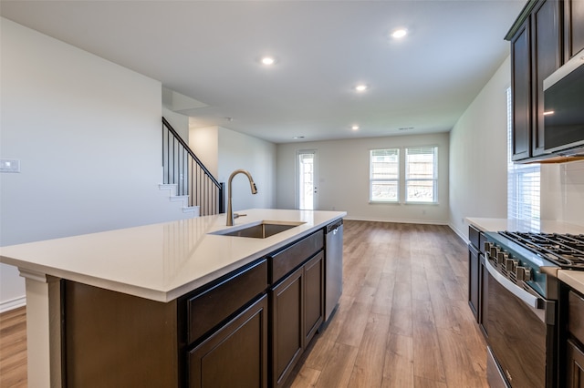 kitchen with sink, light wood-type flooring, a center island with sink, dark brown cabinets, and appliances with stainless steel finishes