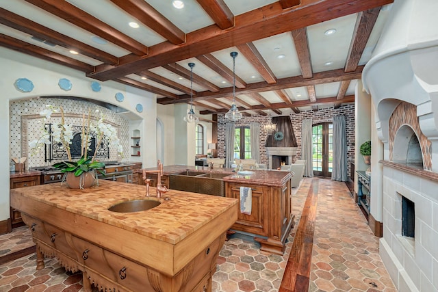 kitchen featuring a kitchen island with sink, sink, beam ceiling, and decorative light fixtures