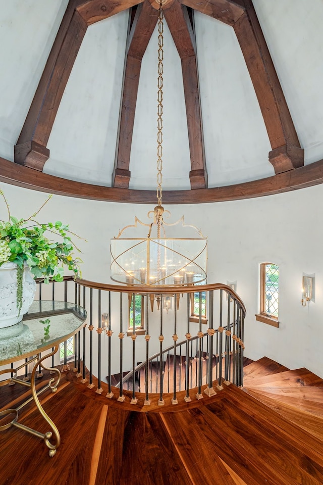 stairway with beamed ceiling, a towering ceiling, a chandelier, and hardwood / wood-style floors