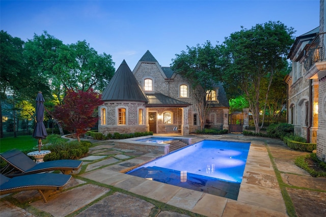 pool at dusk featuring a patio area and an in ground hot tub