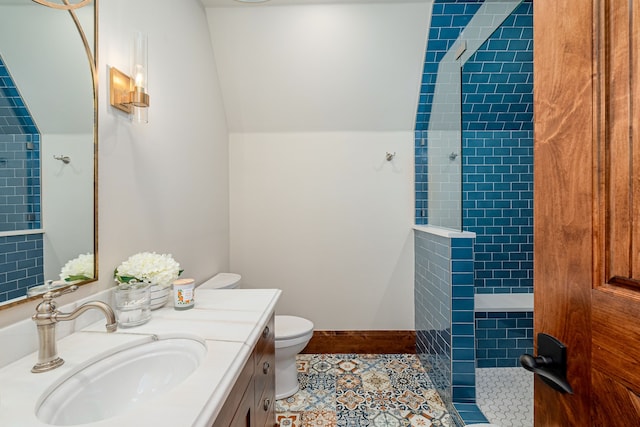 bathroom with a tile shower, lofted ceiling, vanity, toilet, and tile patterned floors